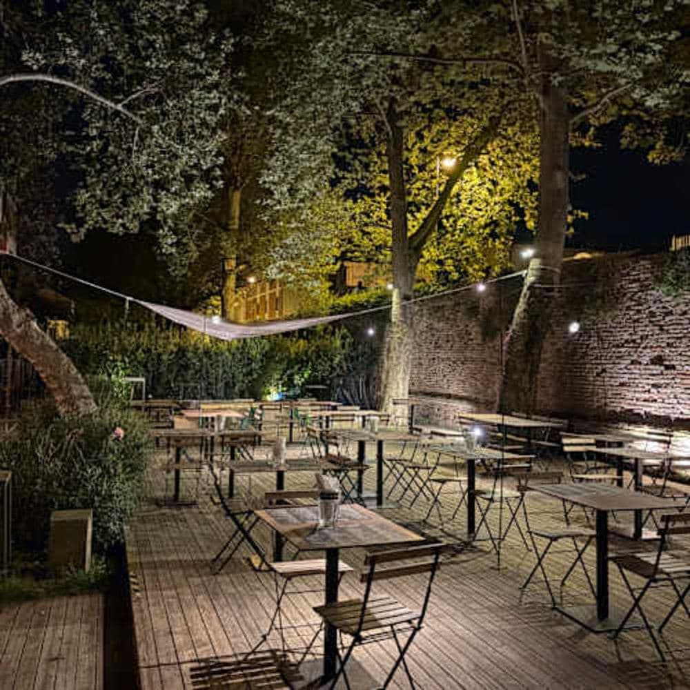 Wooden tables and chairs under the trees at Porta Galliana - Club Primo Piano, Rimini, with lights hanging from the branches