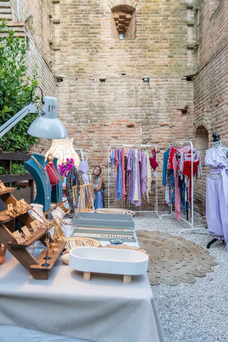 The courtyard of Al Giardino Segreto with rails of colourful clothes, a jewellery stand and brick walls