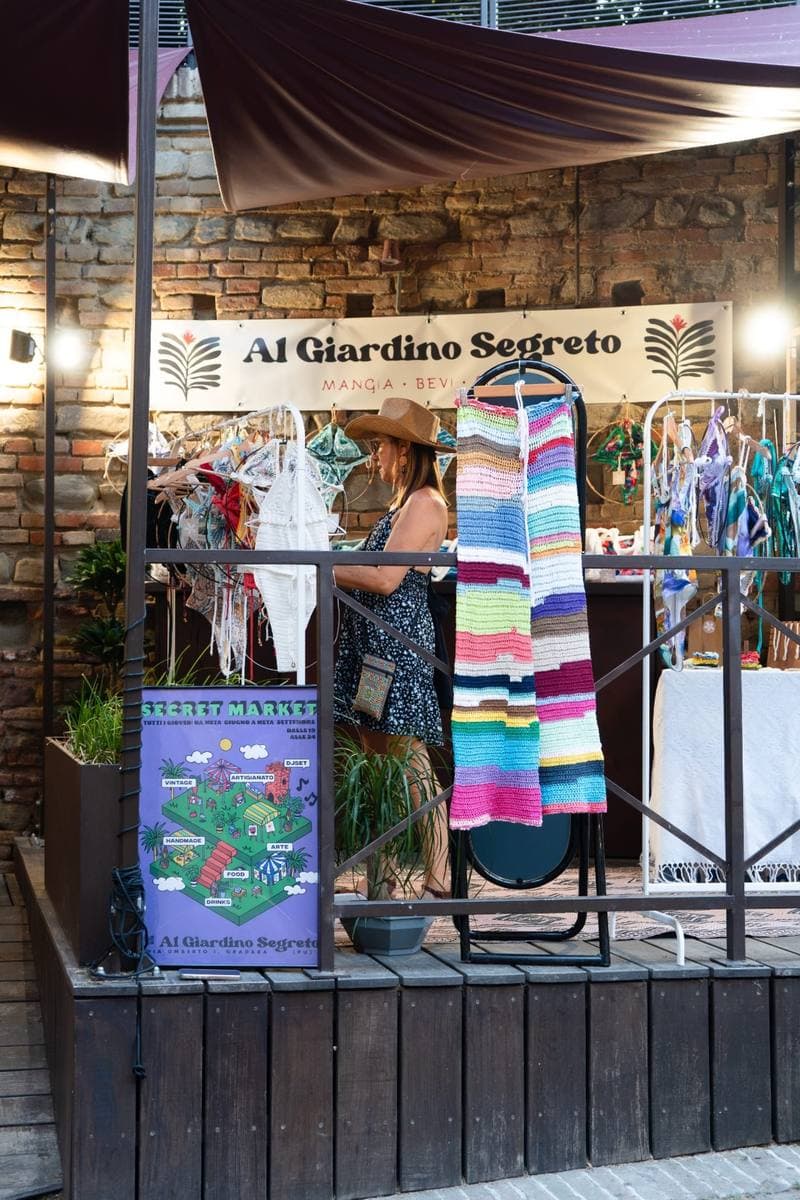 The entrance of Al Giardino Segreto in Gradara with its sign, a burgundy awning and a striped scarf hanging from a display