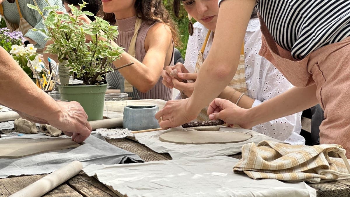 Un tavolo apparecchiato per un laboratorio di ceramica all'aperto, in un giardino, con ciotole e attrezzi pronti