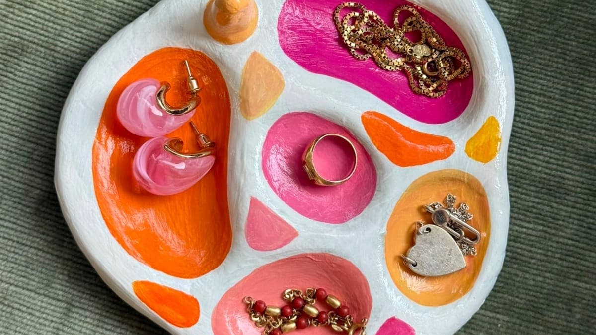 A hand-painted ceramic jewellery dish in pink and orange, with rings and earrings resting on it
