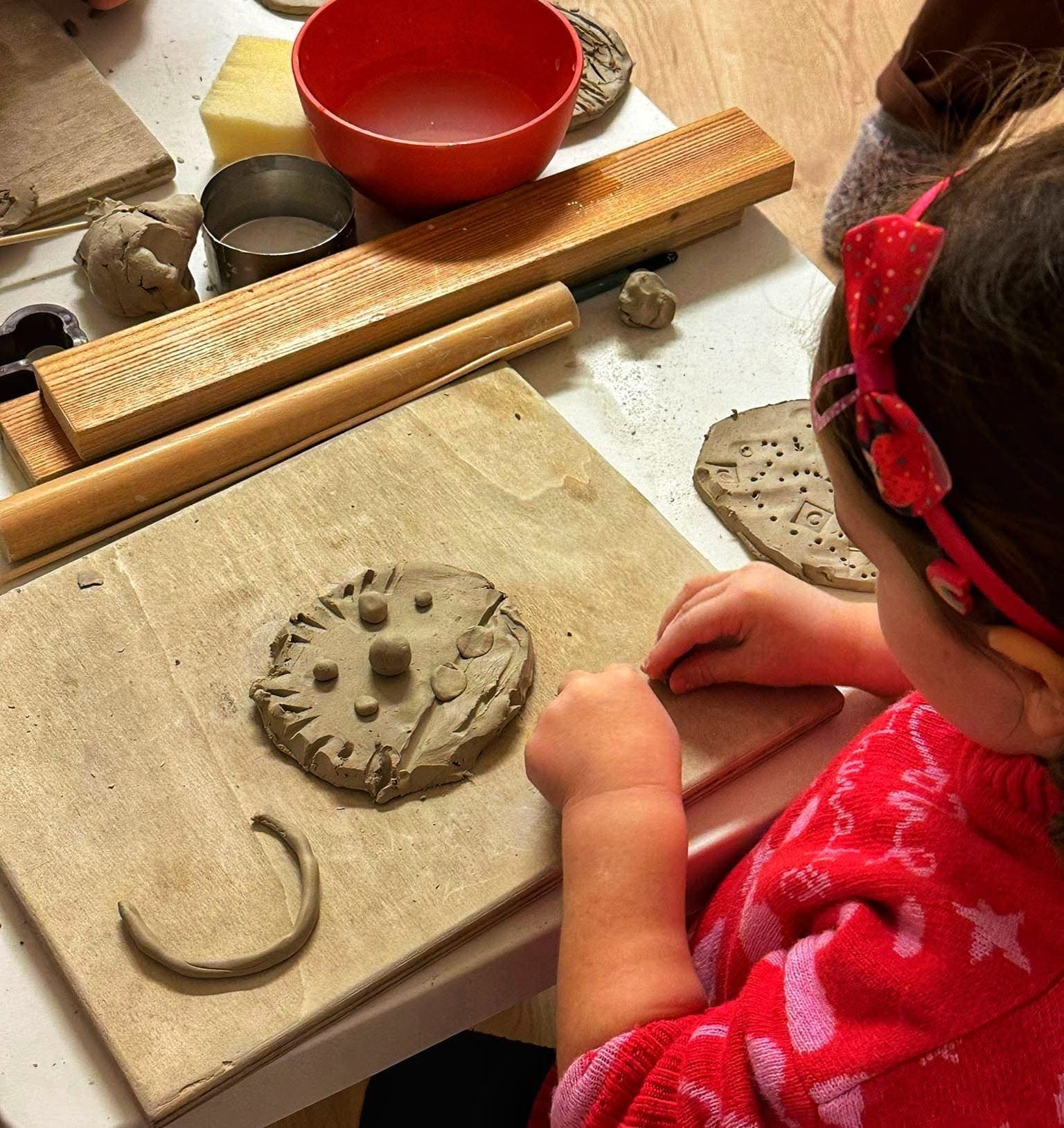 A little girl shaping a clay disc with small raised details on a wooden board